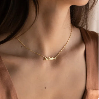 Gold necklace with 'Natalie' pendant on a person wearing a brown top.