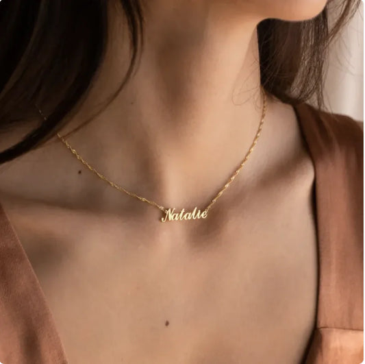 Gold necklace with 'Natalie' pendant on a person wearing a brown top.